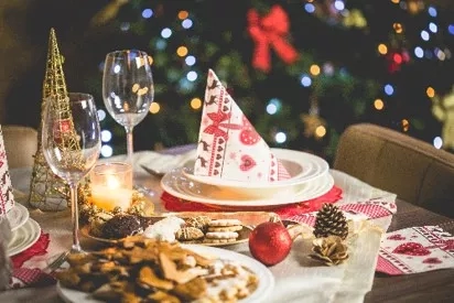 A table set for a holiday dinner with festive decorations and a Christmas tree in the background.