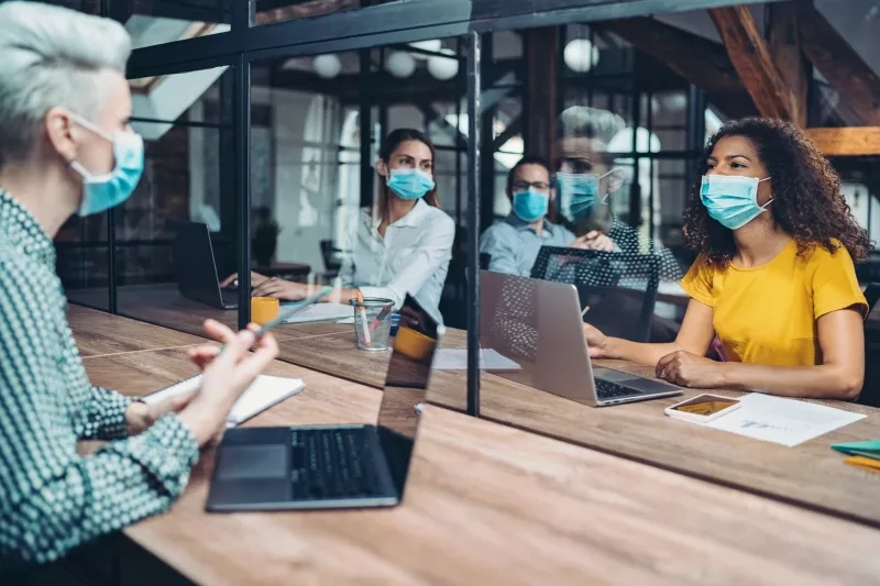 Office meeting with glass partition and people wearing masks in the COVID-19 pandemic.