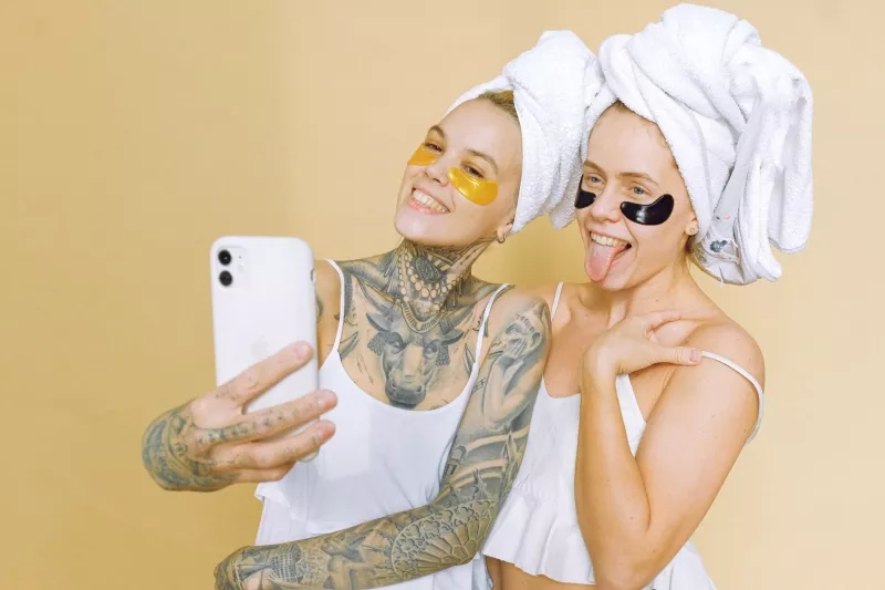 Two women in bathrobes and face masks take a selfie at a spa.