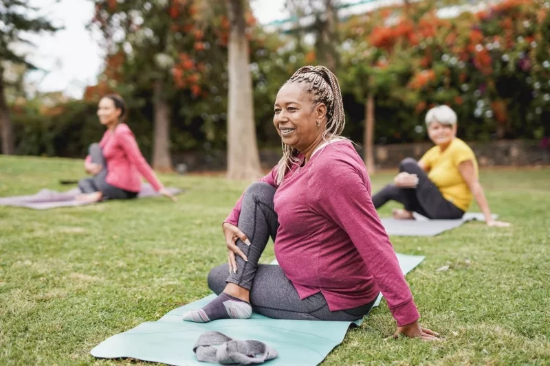 Three women sitting on yoga mats doing yoga in the park.