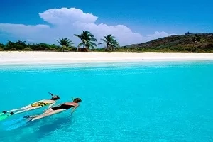 Two people are snorkeling in the clear blue water of Anguilla Beach.