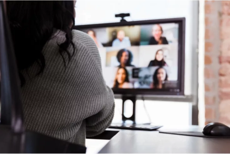 Woman on video call with colleagues, with focus on screen displaying diverse team members in a virtual meeting.
