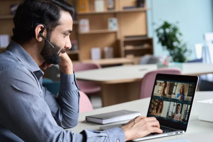 Man using a headset on a laptop for a video call with colleagues in an office.