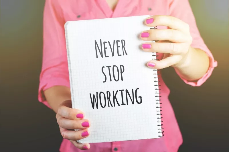 A woman holds a notebook that says never stop working in black letters on a white background.