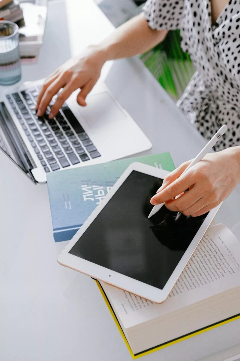 A woman is using a laptop and tablet to work on her blog in her home office.