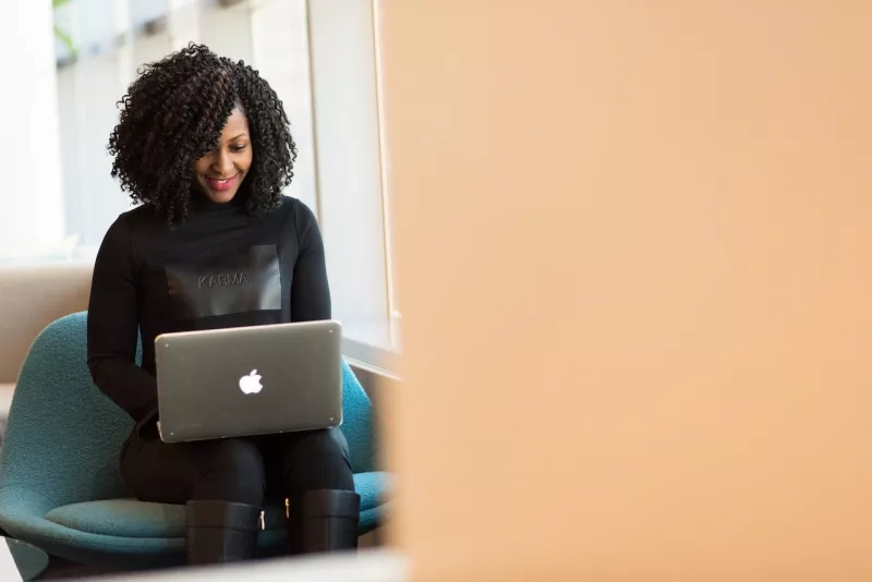 A woman with curly hair is sitting on a chair and using a laptop with the Apple logo.