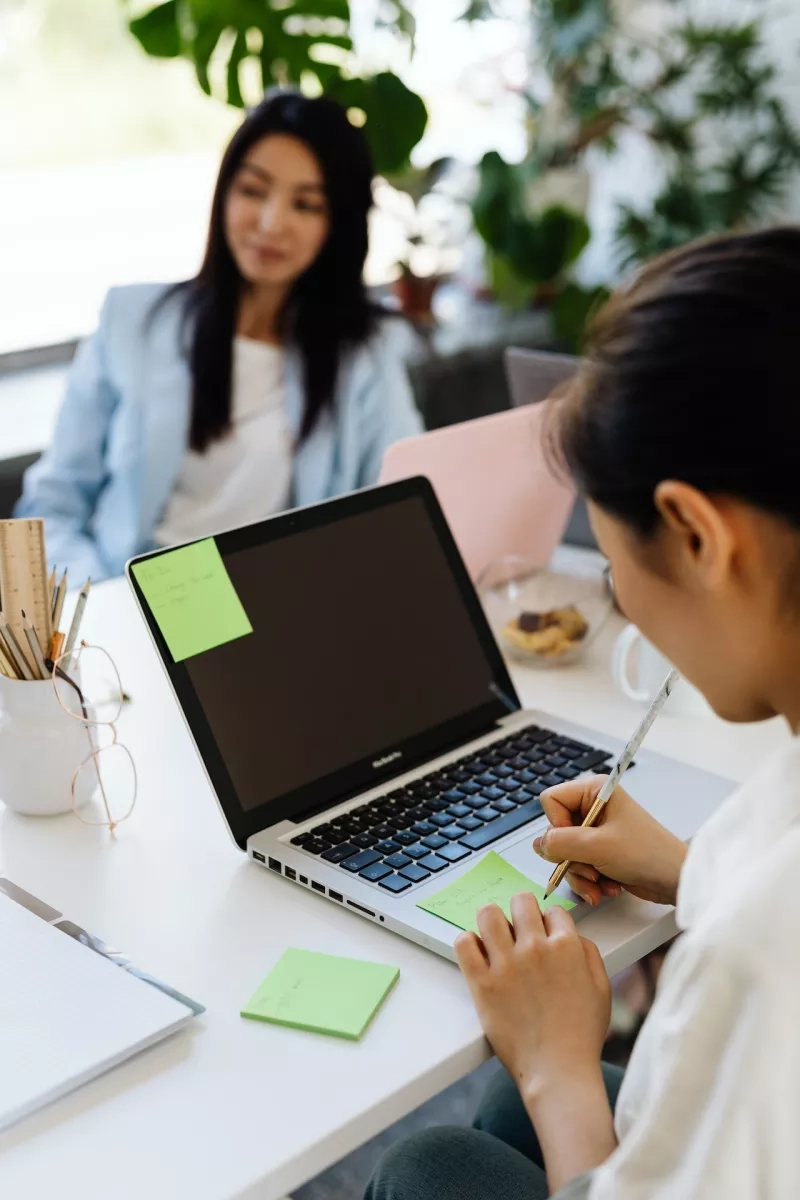 Two women working in an office with post-it notes and a laptop on the table.