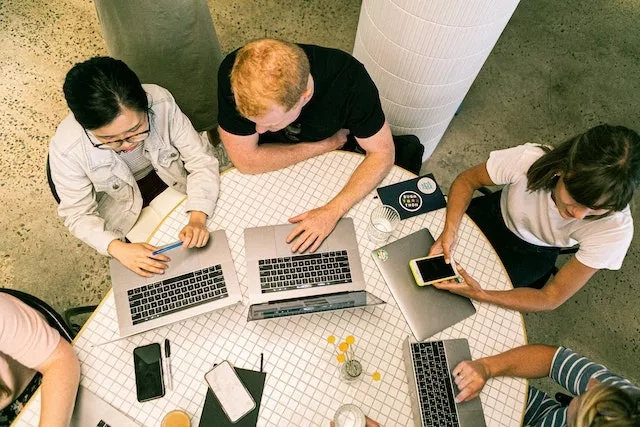 A group of people are working on laptops, a glass of water, and a cup of coffee on a table.