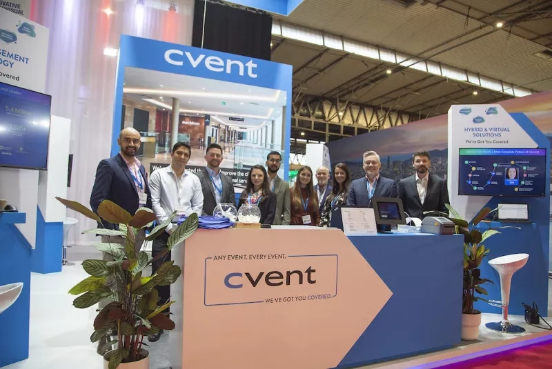 A group of people standing behind a counter with a Cvent logo at an event stand.