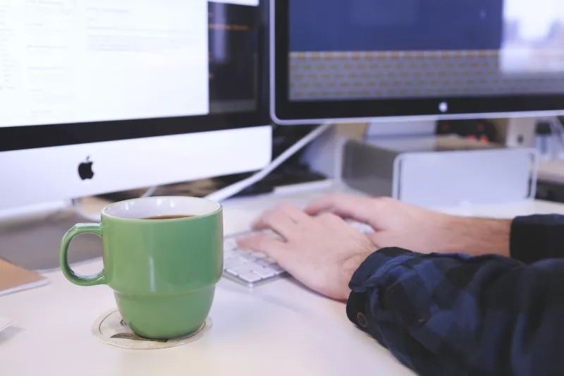 A man typing on a keyboard with a green mug on the table.