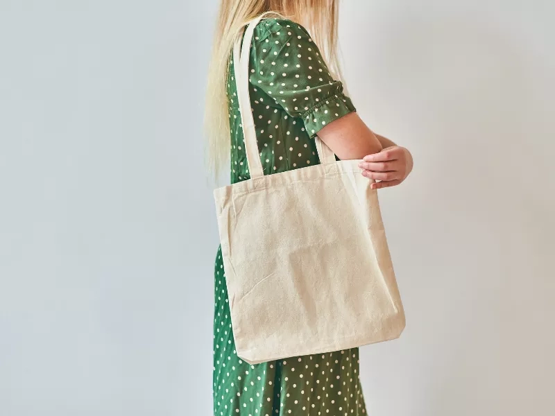A woman in a green dress is carrying a white tote bag in her right hand.