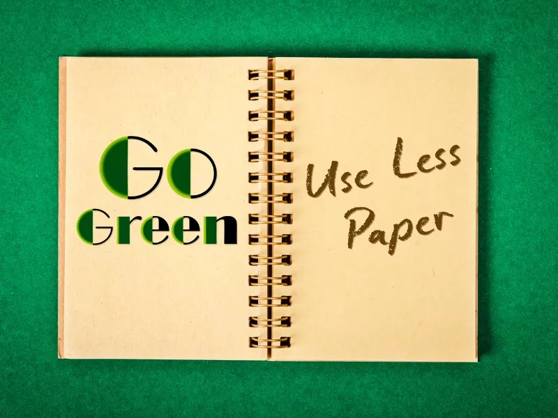 An open notebook with the text "Go Green" and "Use Less Paper" handwritten on it.