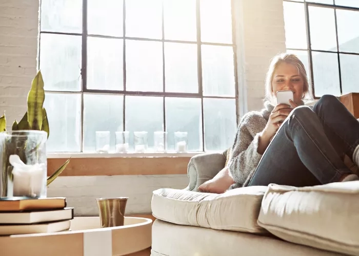 Woman sitting on a couch looking at her phone while relaxing in a loft-style living room.