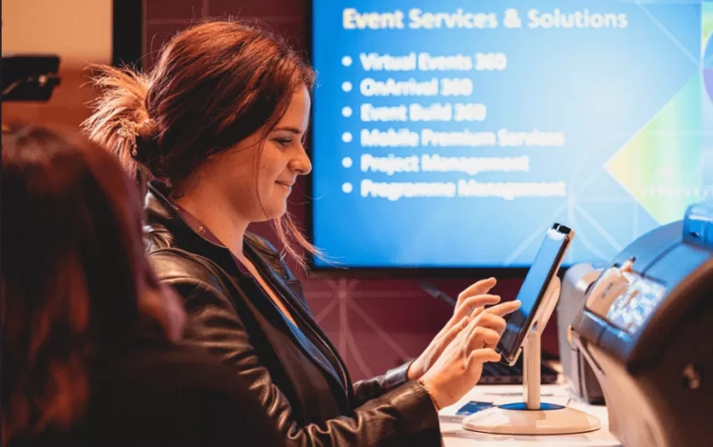 A woman is using a tablet in front of a monitor showing event services and solutions.