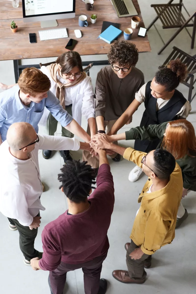 Group of eight people at a meeting, placing hands in a circle to symbolize unity.