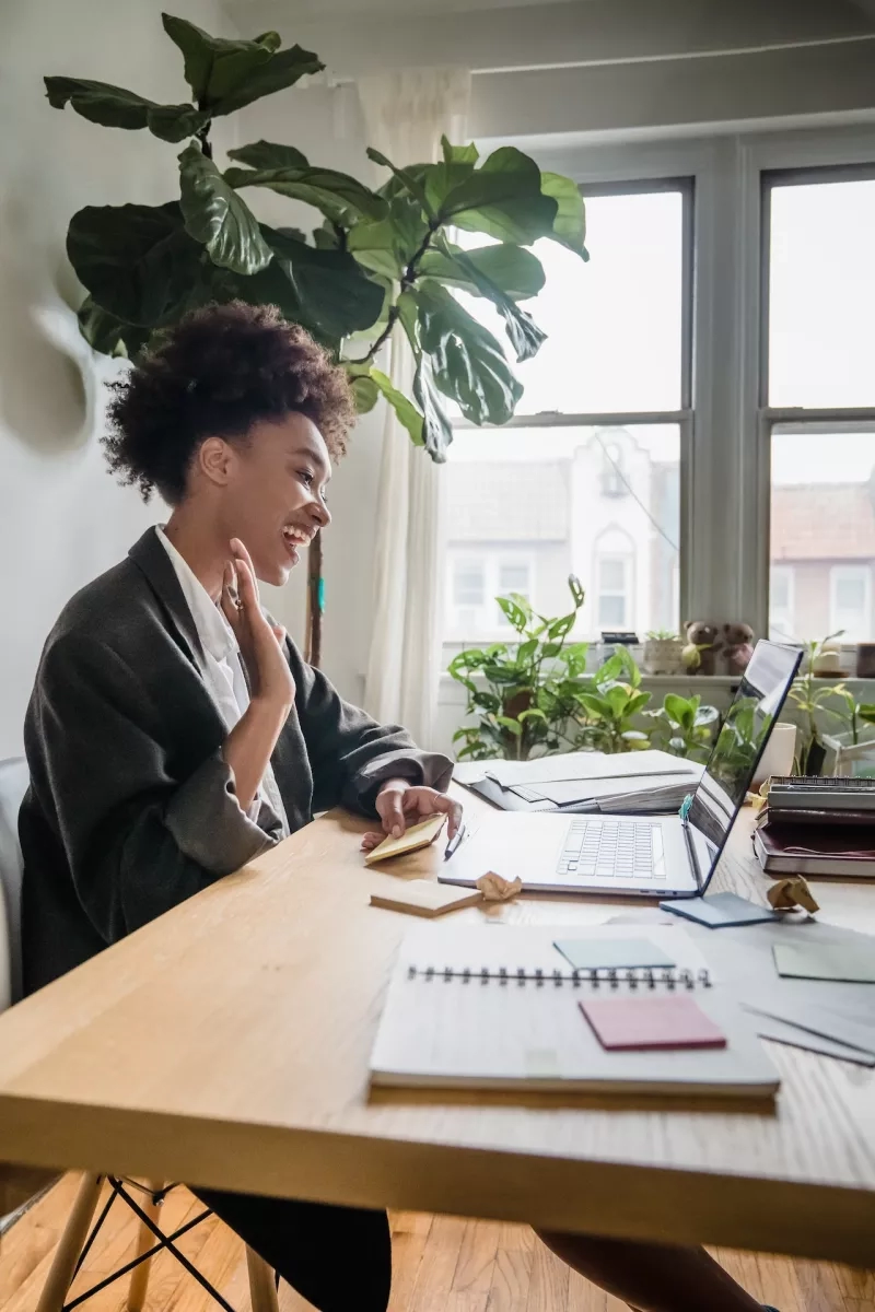 A woman sitting in her home office is laughing while working on her laptop computer.