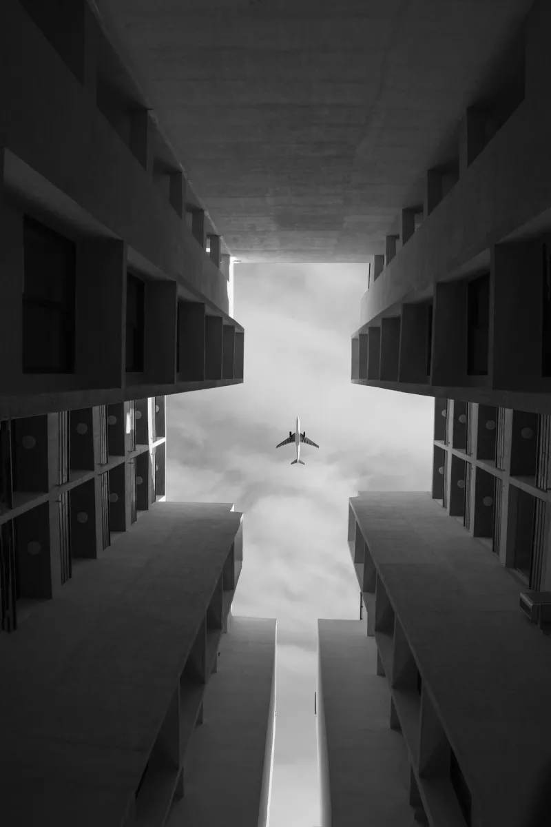 A plane flies through a concrete building in a black and white image.
