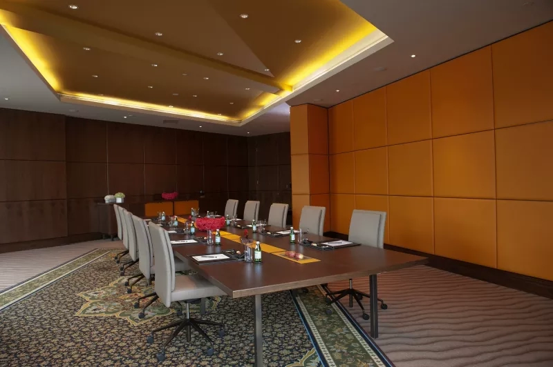 Jumeirah Creekside Hotel - Meeting room with beige chairs, table, and orange walls, and a carpeted floor.