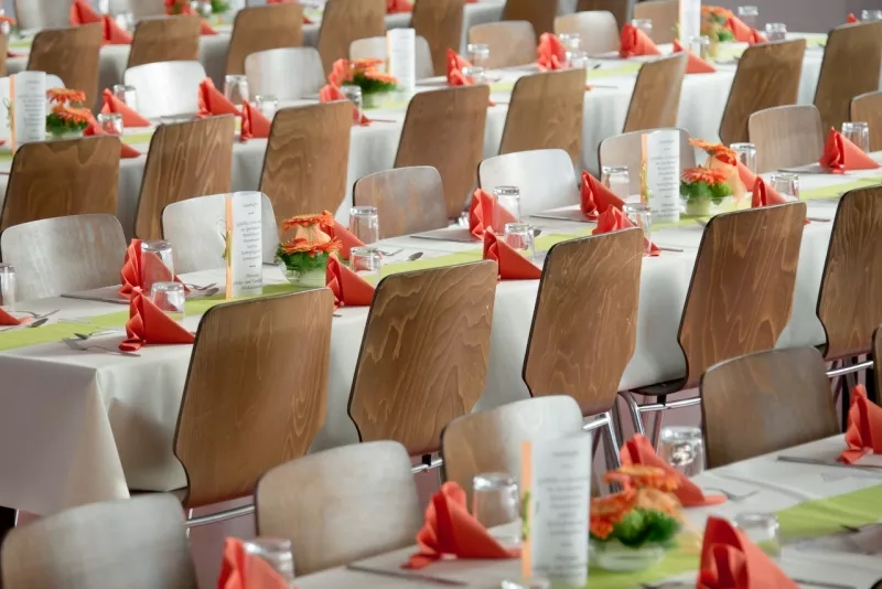 An event table with white tablecloth, orange napkins, and orange flowers in the middle of each table.