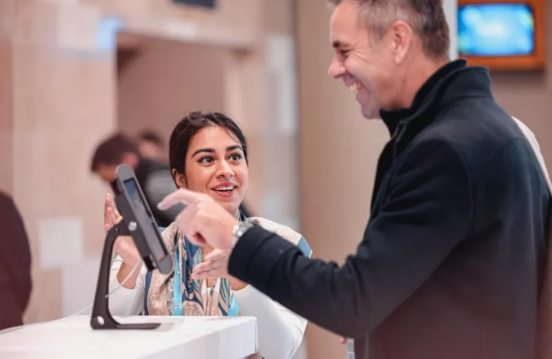 A man and a woman laughing together in front of a monitor at a registration counter.