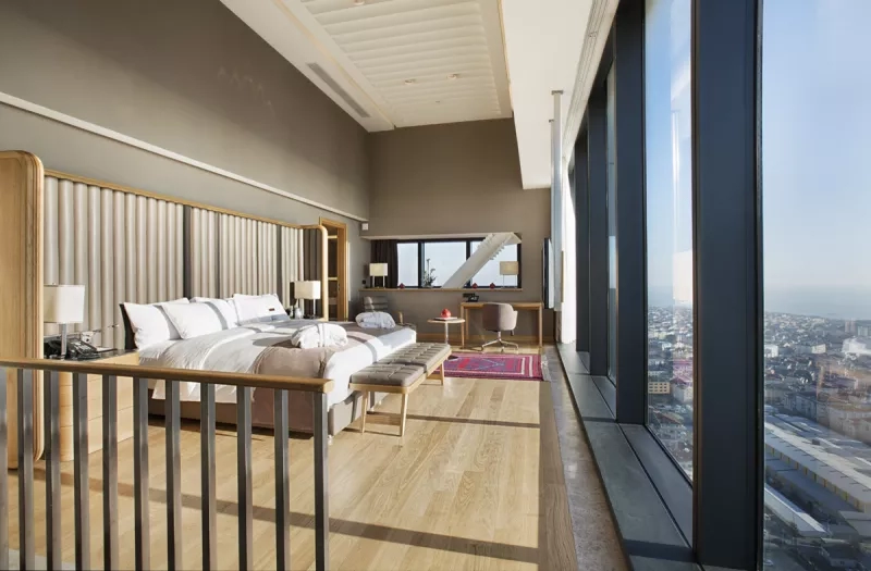 A view of a spacious hotel room with a king-sized bed and a city view from the windows.