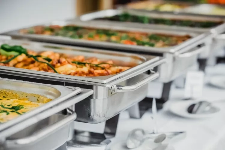 Stainless steel trays with hot food arranged on a table for a buffet service at a wedding.
