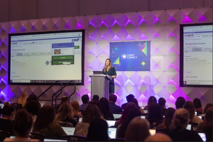 A lady is standing on the podium in front of the audience and talking to them.