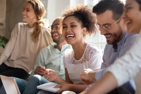 Group of friends are sitting together and laughing while one woman holds a notebook and pen.