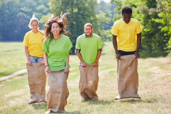 Four people participating in a sack race outdoors with trees and grass in the background.