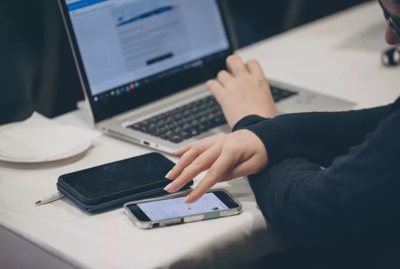 Person using a laptop and mobile phone on a desk, with a webinar checklist on the screen.