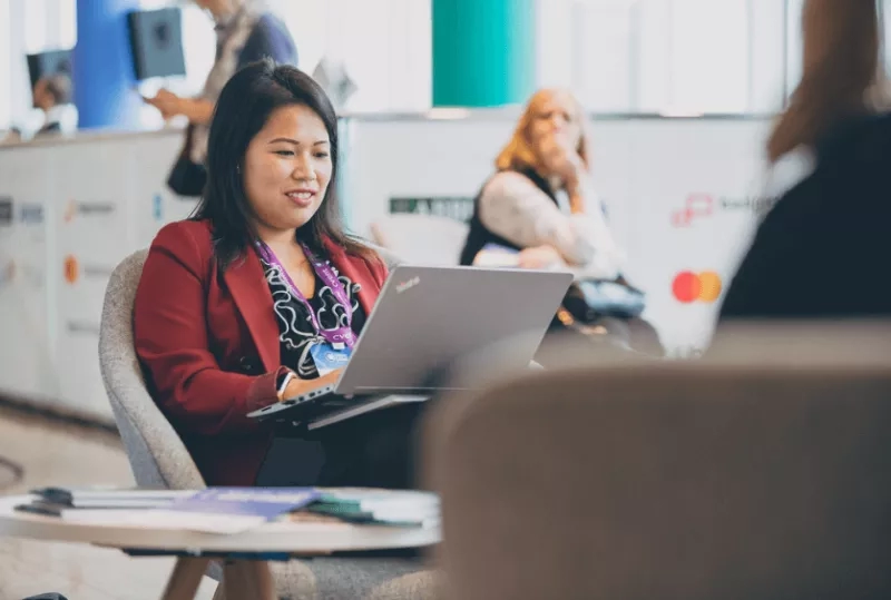 A woman is sitting on a chair and working on her laptop at the CVENT booth.