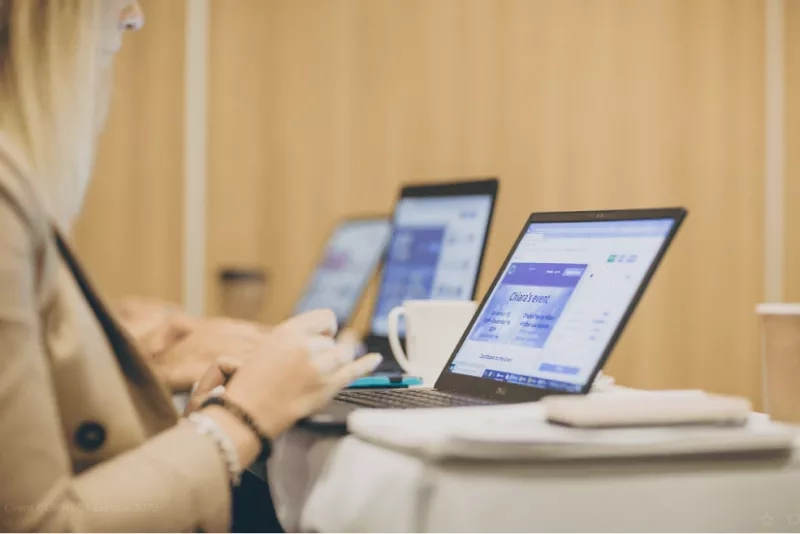 Woman at a meeting with a laptop open to an event page.