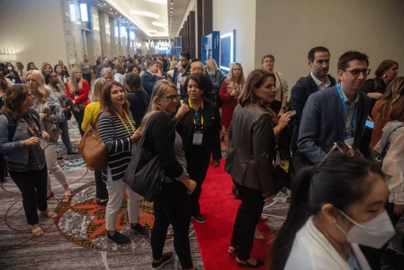 Many people at an event with a red carpet and blue walls on the side.