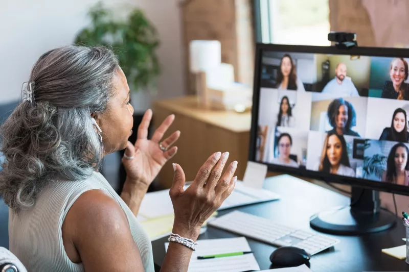 Woman attending a virtual corporate event in an office with a computer and people on the screen.