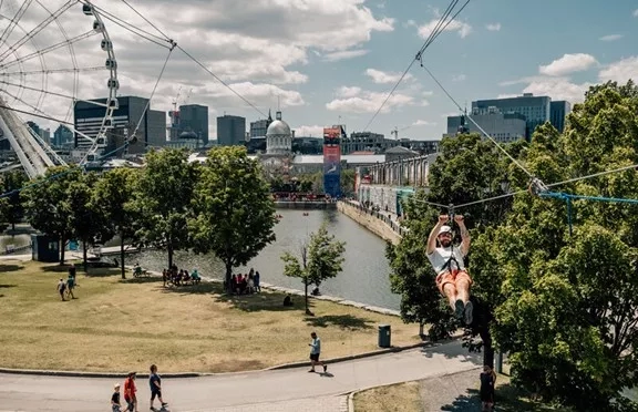 A man riding the zipline in the Montreal area with a Ferris wheel and cityscape in the background.