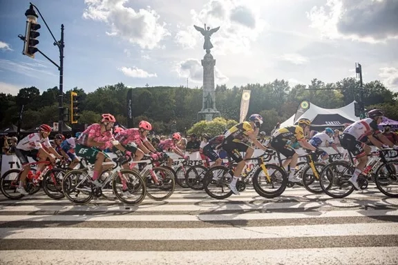 Cyclists ride their bikes in a marathon with tents and traffic lights in the background.