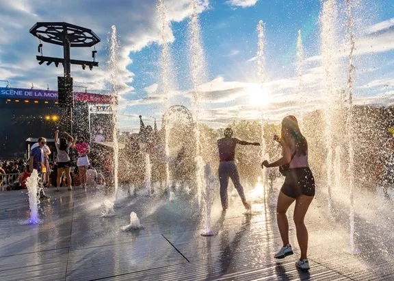 Water jets at Osheaga music festival with people dancing and the sun setting in the background.