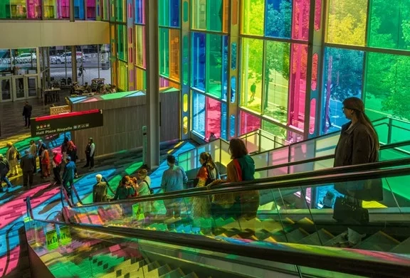 Escalators leading to the entrance of the Montreal Museum of Fine Arts, illuminated by colorful stained glass windows.