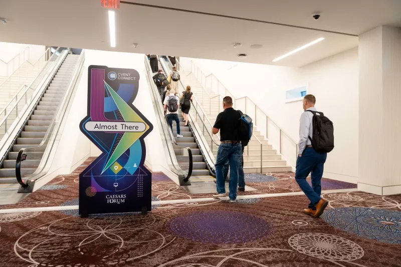 Two escalators with people on them next to an Almost There sign with two men standing in front.