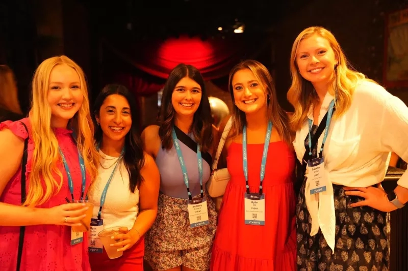 Five women in a group smiling, wearing name tags with the text "event" written on them.