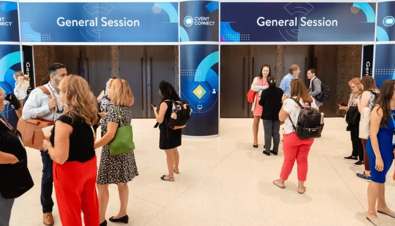 People gathered in a conference room with "General Session" posters on the wall.