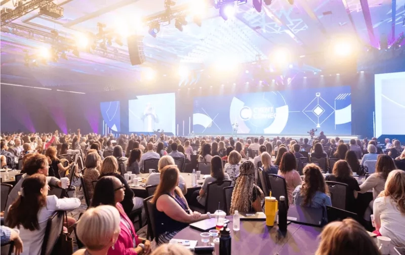 A conference with hundreds of people, a big stage, and three big screens.