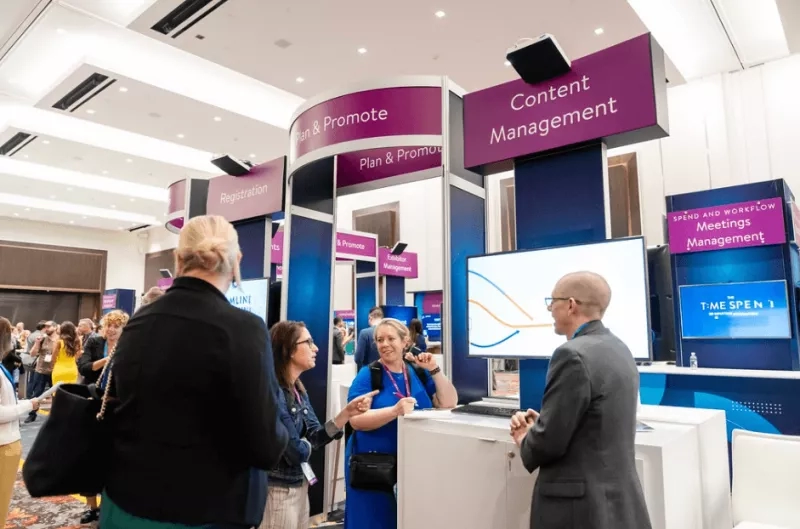 A conference expo with people gathered around a stand that says "Content Management" and a monitor.