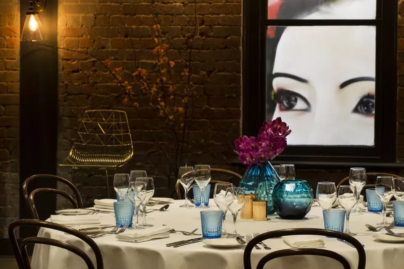 A dining table with plates, cutlery, and wine glasses set in front of a window with a woman's face.