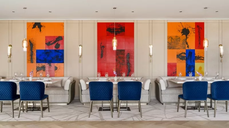Tang Court restaurant with vibrant red and orange paintings and blue chairs around the tables.
