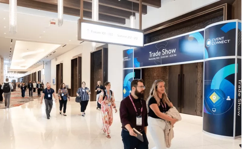 A group of people are walking in a corridor with the sign "Trade Show" in front of them.