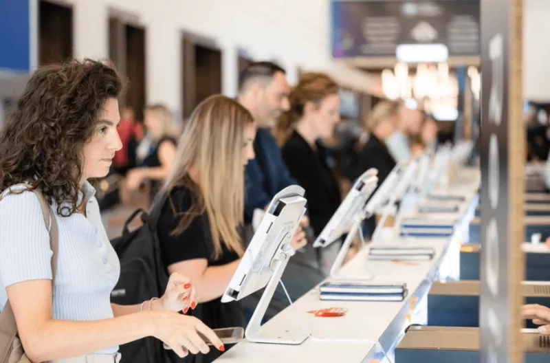 A group of people standing in a queue at an expo management counter and using a tablet.