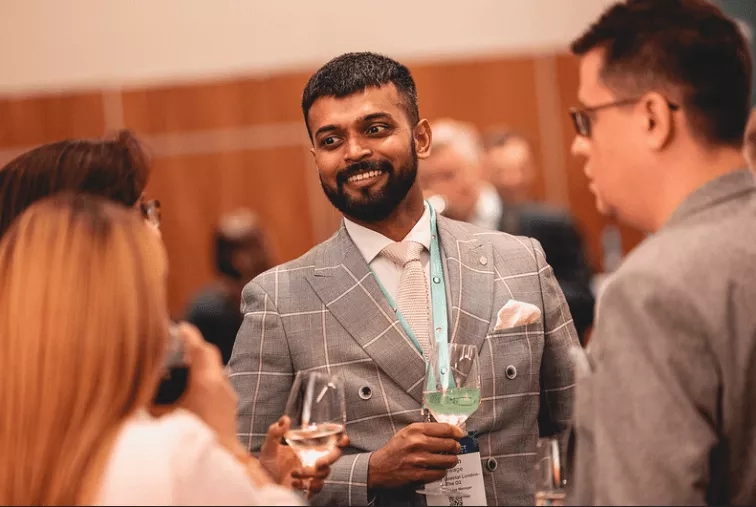A man holding wine glass while talking to others at a networking event.
