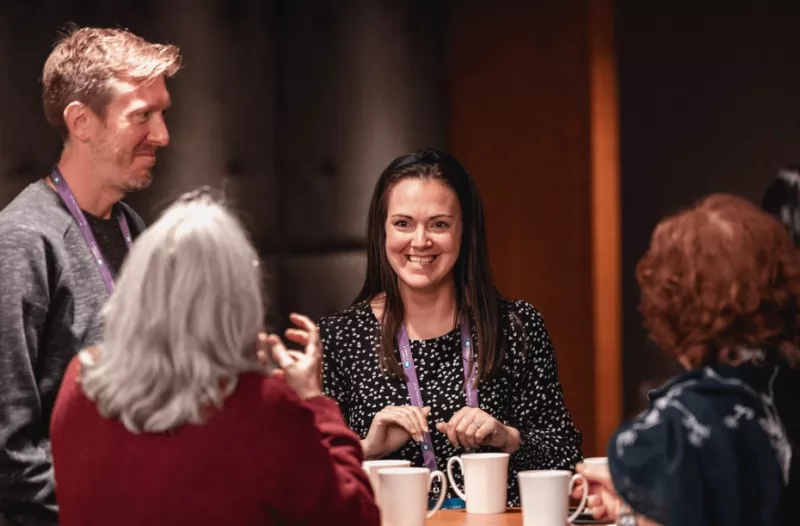 Group of four people at a table with coffee cups, having a conversation.