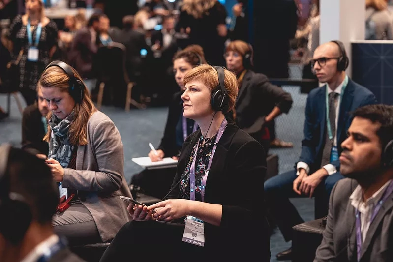 People wearing headphones at a tech conference with a woman holding a phone in the foreground.
